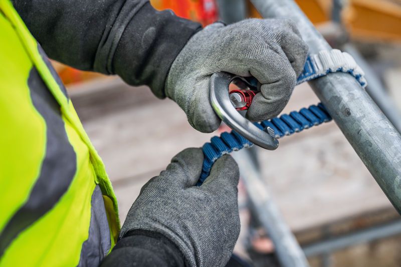 Une personne portant un équipement de sécurité fixe une longe d'escalade à un échafaudage.