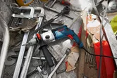 Perceuse à percussion avec poignée auxiliaire placée sur un établi en métal parmi des outils dispersés.