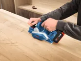Personne utilisant une raboteuse sans fil pour lisser une surface en bois.