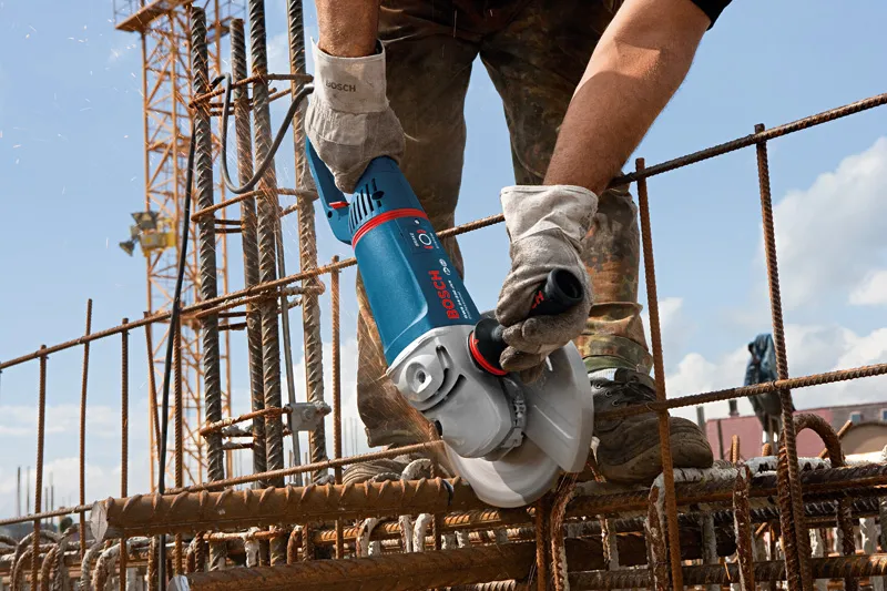 Une personne portant un équipement de sécurité coupe des barres d'armature sur un chantier de construction avec une meuleuse d'angle.
