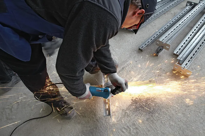 Une personne portant un équipement de sécurité broie une poutre métallique, produisant des étincelles brillantes.