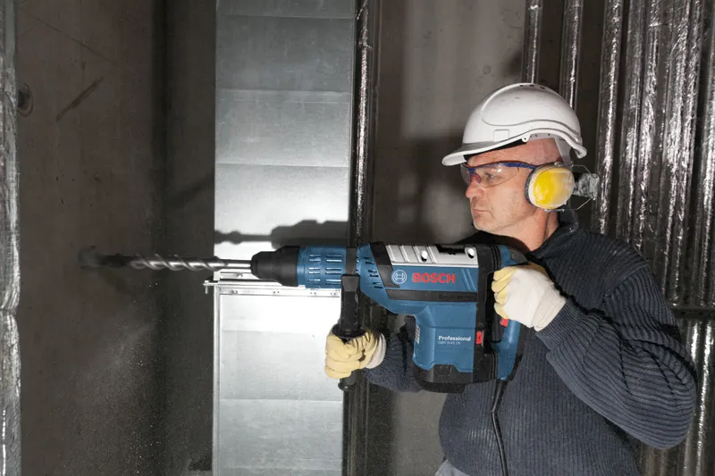 Une personne portant un équipement de sécurité perce un mur en béton à l’aide d’un marteau perforateur.