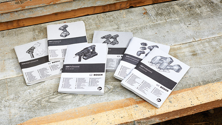 Cinq manuels Bosch Professional posés sur un plan de travail en bois brut.