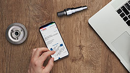 Une main utilise un smartphone à côté d'un ordinateur portable et d'un engrenage.