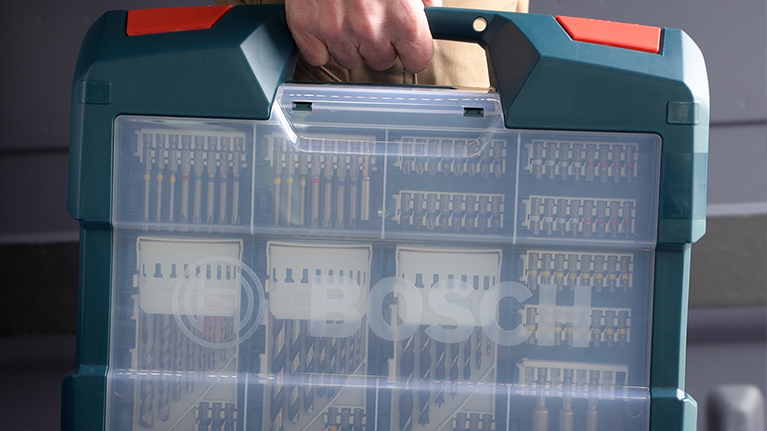 Une mallette Bosch avec des outils et accessoires visibles, tenue par une main.