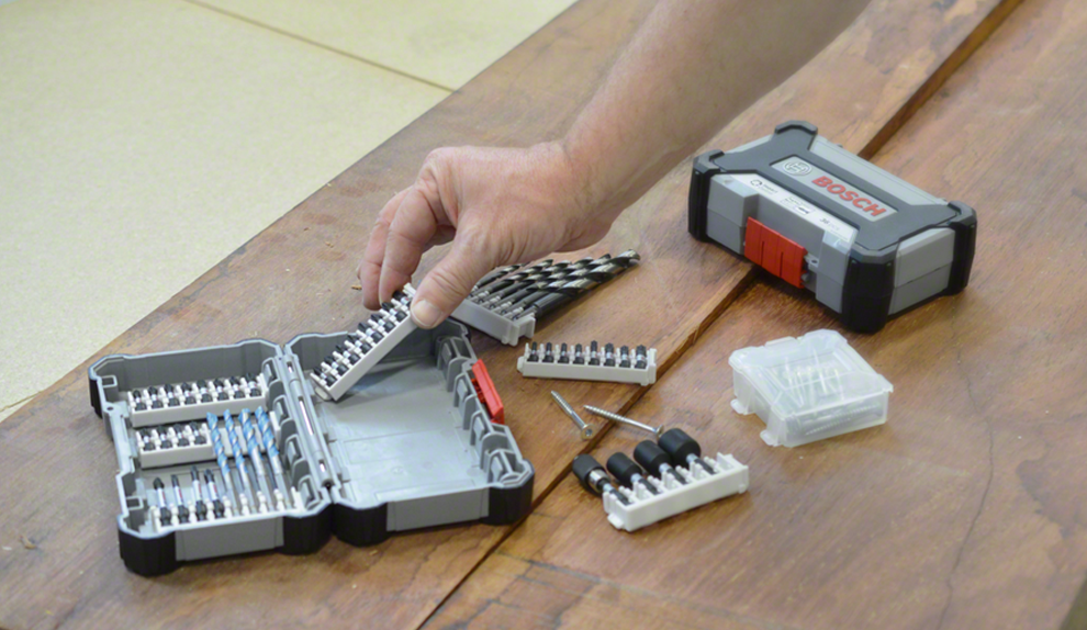 Un homme sort des embouts d'un coffret Bosch sur une table en bois.