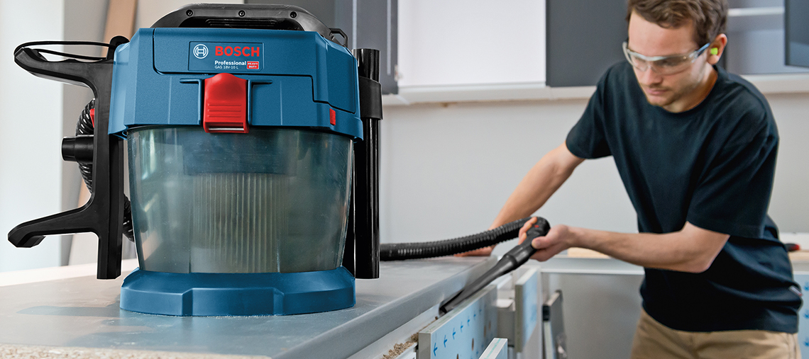 Un aspirateur Bosch Professional bleu sur un plan de travail, un homme nettoie.