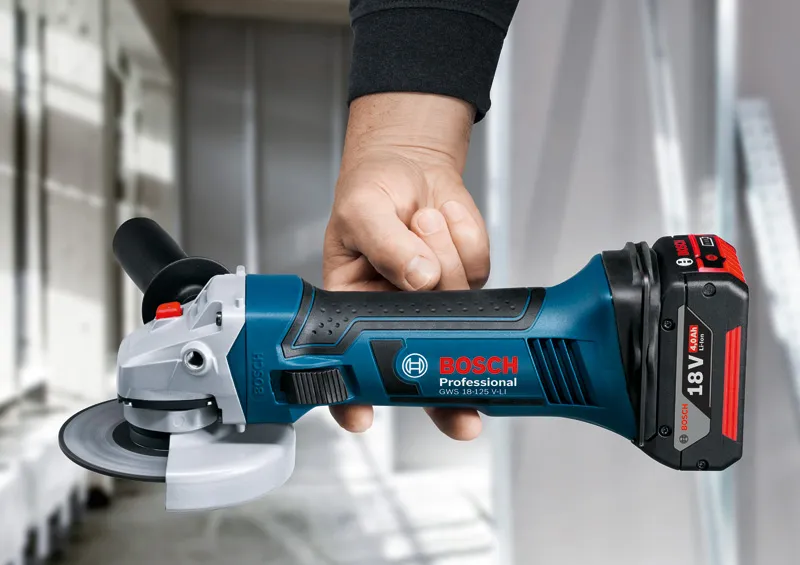A person holds a cordless angle grinder inside a workshop.