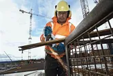 Person wearing safety equipment uses an angle grinder to cut metal rods on a construction site.