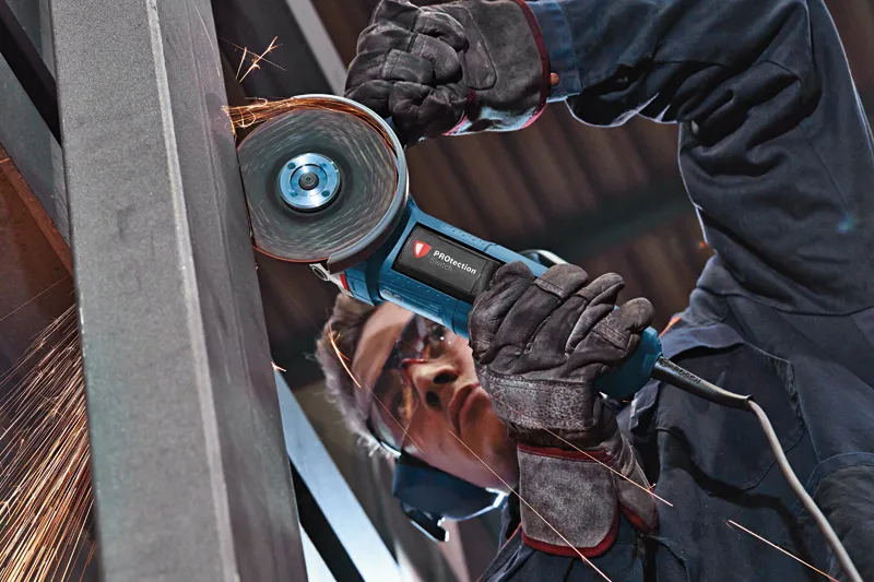 A person wearing safety equipment grinds metal with an angle grinder, creating sparks.
