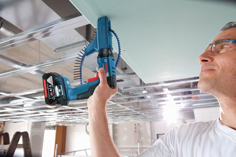 A person wearing safety equipment drives screws into a ceiling with a cordless screwdriver.