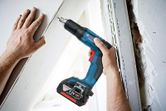 A person drives screws into drywall using a cordless screwdriver.