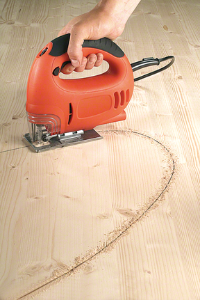 A jigsaw is cutting a curved line in a wooden panel.
