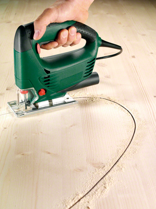 Person guides a green jigsaw, cutting a curved line in a wooden board.