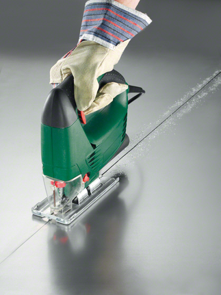 A person wearing safety equipment uses a jigsaw to cut a straight line in sheet metal.
