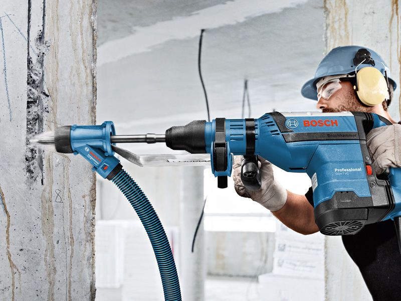 A person wearing safety equipment drills into concrete with a rotary hammer and dust extraction.