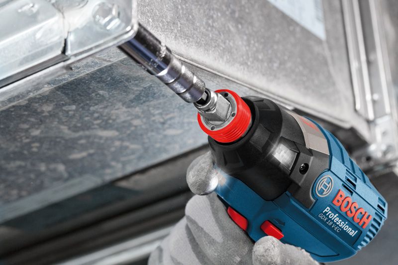 A person wearing safety equipment uses a cordless impact wrench to fasten a metal frame.