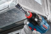 A person wearing safety equipment uses a cordless impact wrench to fasten a metal frame.
