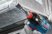 A person wearing safety equipment uses a cordless impact wrench to fasten a metal frame.