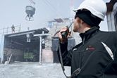 A person wearing safety equipment communicates with a radio at a busy construction site.