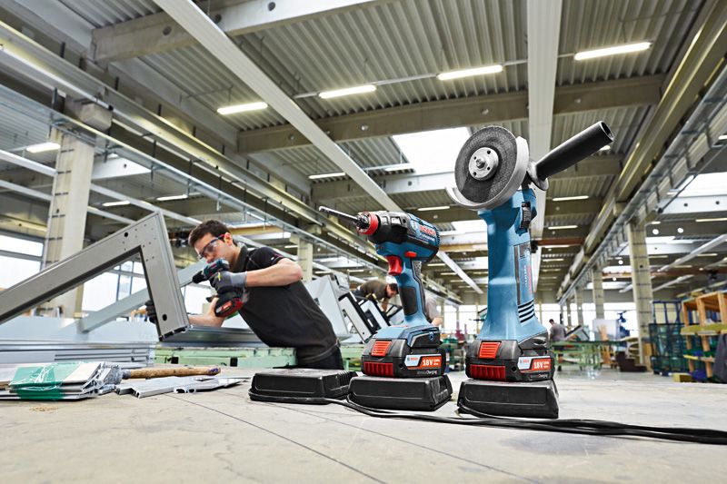 A person wearing safety equipment uses a cordless tool in a large industrial workspace.