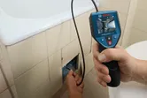 Person using an inspection camera to examine inside a tiled wall panel.