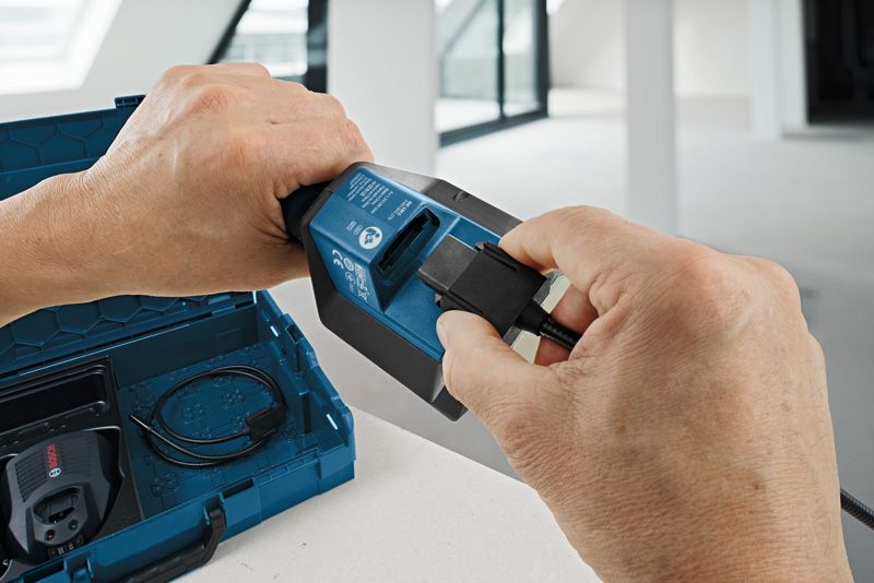 A person connects a charging cable to a power tool battery next to an open case.