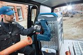 A person wearing safety equipment holds a cordless tool inside a work van at a construction site.