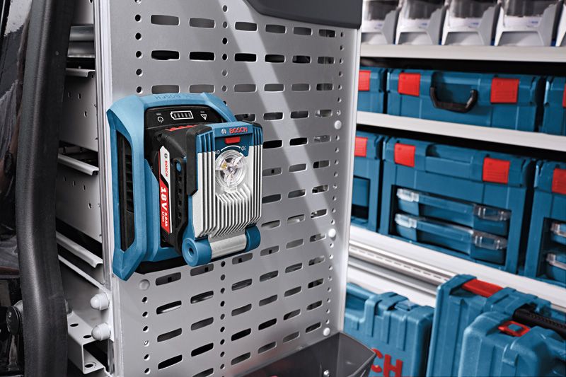 Cordless work light mounted on a perforated metal panel in a workshop storage area.