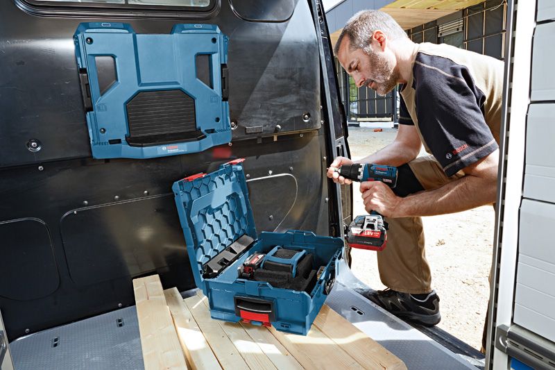 A person using a cordless power drill beside an open tool case in a work van.