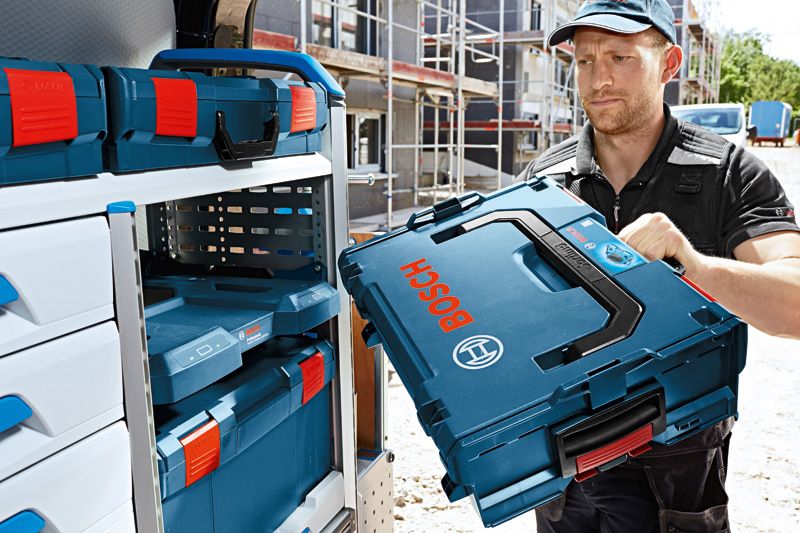 A person loads a blue tool case into a storage shelf on a construction site.