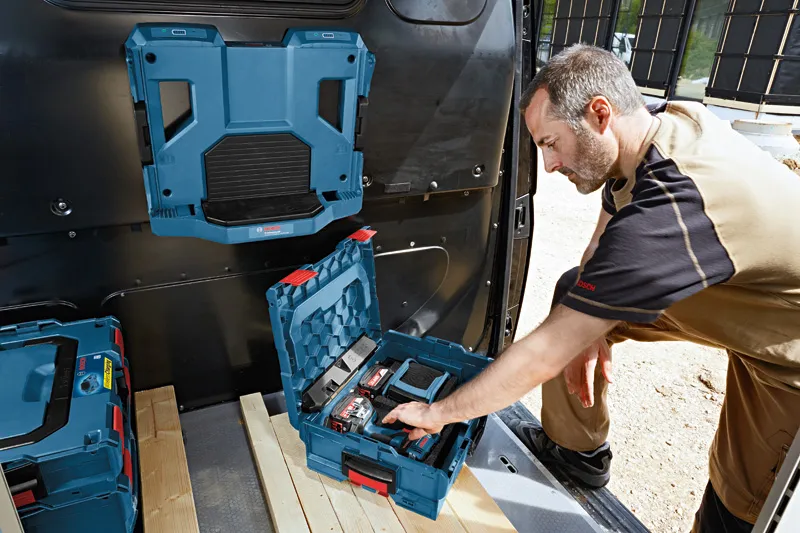 A person organizes power tools and batteries in a blue carrying case inside a vehicle.