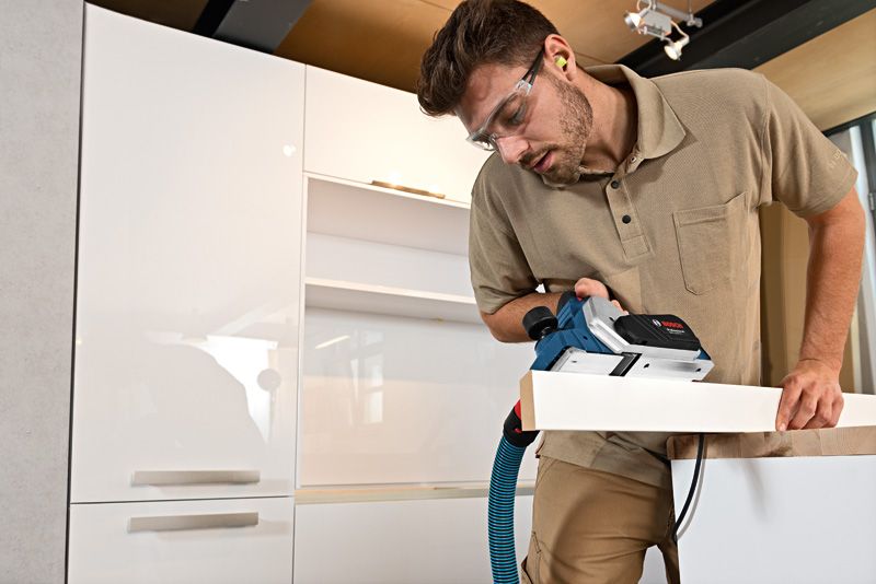 A person wearing safety equipment uses a planer on a wooden board.