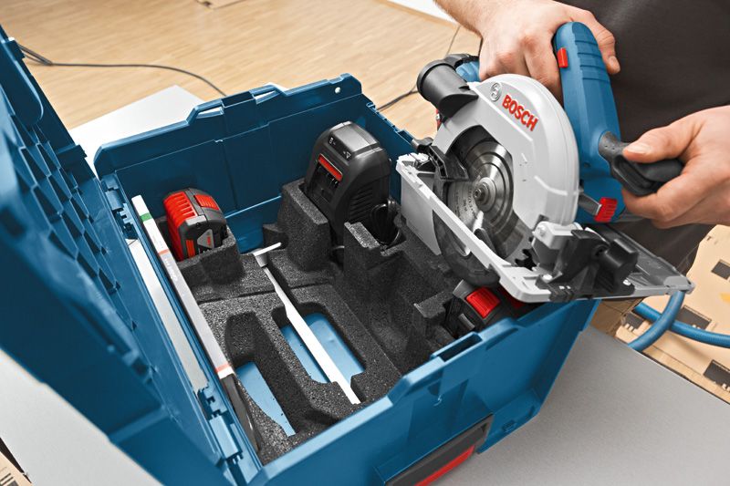 A person places a cordless circular saw into a carrying case with battery and charger.