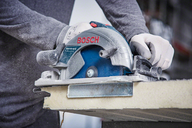 Person wearing safety equipment cuts a board using a circular saw.