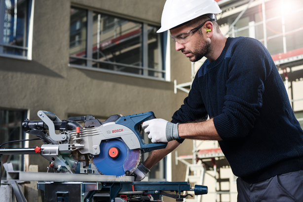 Worker wearing safety equipment cuts wood with a circular saw at a construction site.