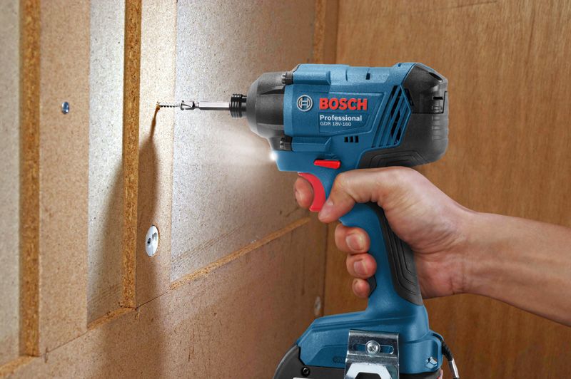 A person drives a screw into a wooden panel using a cordless impact driver.