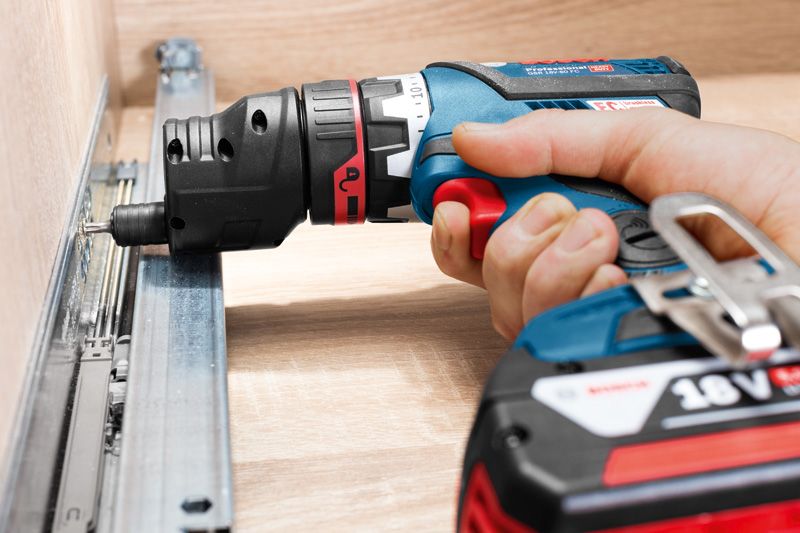 A person drives a screw into a metal drawer rail using a cordless drill.