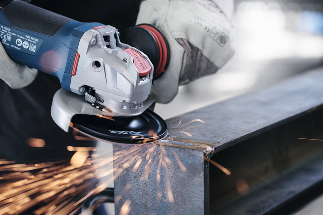 A person wearing safety equipment grinds a metal beam with an angle grinder.