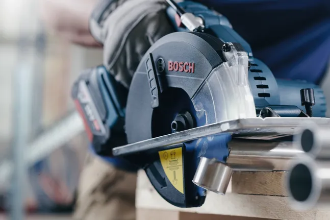 Person wearing safety equipment uses a circular saw to cut metal pipes.