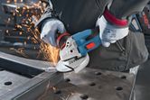 A person wearing safety equipment grinds metal with a cordless angle grinder.