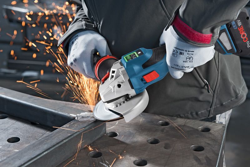 A person wearing safety equipment grinds a metal beam with a cordless angle grinder.