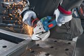 A person wearing safety equipment grinds a metal beam with a cordless angle grinder.