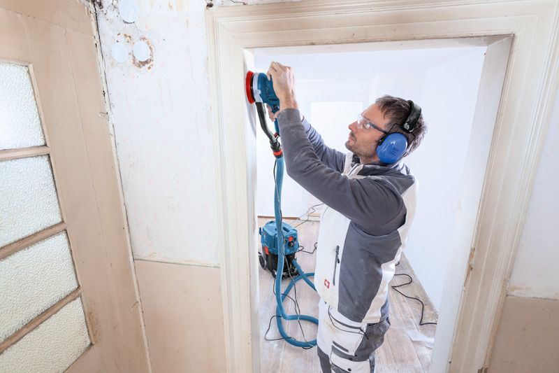 Person wearing safety equipment sands a door frame with a random orbit sander.