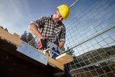 A person wearing safety equipment cuts a wooden beam with a cordless circular saw.
