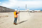 Person wearing safety equipment aligning a laser receiver with a laser leveling tool on a construction site.