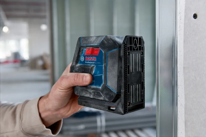 Person uses a laser leveling tool against a metal wall frame indoors.