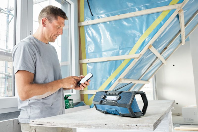 A person adjusts a phone near a blue worksite radio on a construction table.