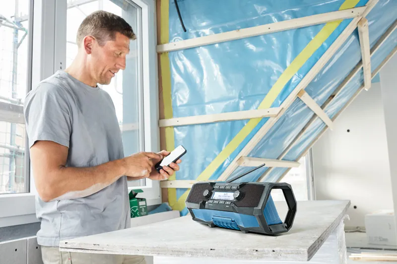 A person using a smartphone beside a portable worksite radio on a construction table.