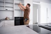 A person installs a shelf in a kitchen, holding a cordless combi drill at their waist.